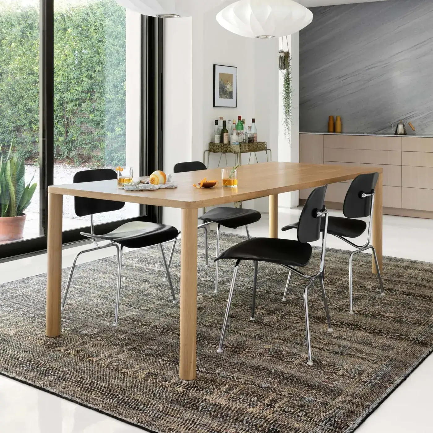 AMARAMM-03CCLJ__5Broomscene_5D_1_1400x Loloi area rug with a traditional gray and brown pattern, under a light wood dining table with black chairs in a modern dining space with large windows.