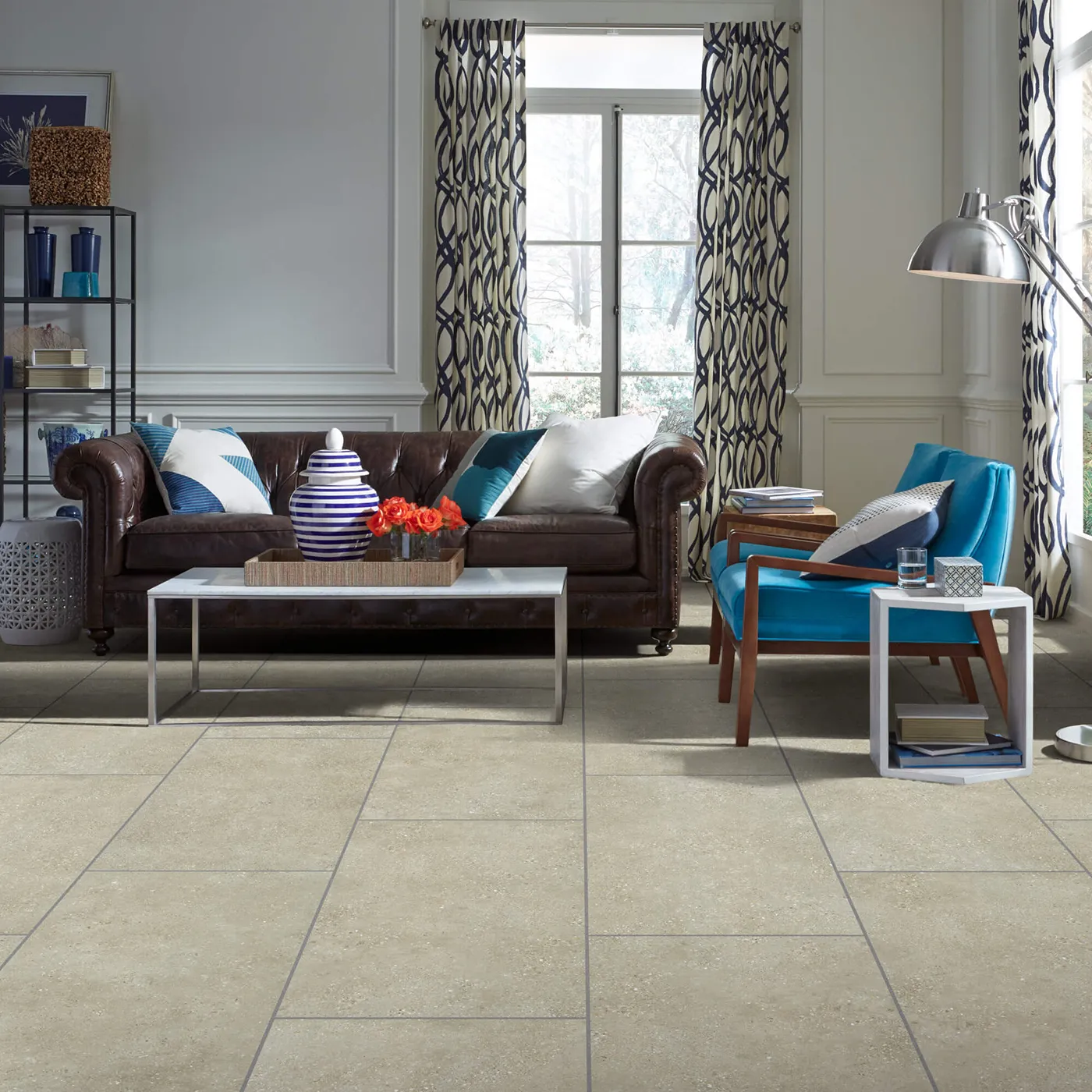 Crete-CS86Q-00200-Cafe-18x36-V Shaw Floors tile in a light beige cafe color, in a living room with a brown leather sofa and blue armchair.