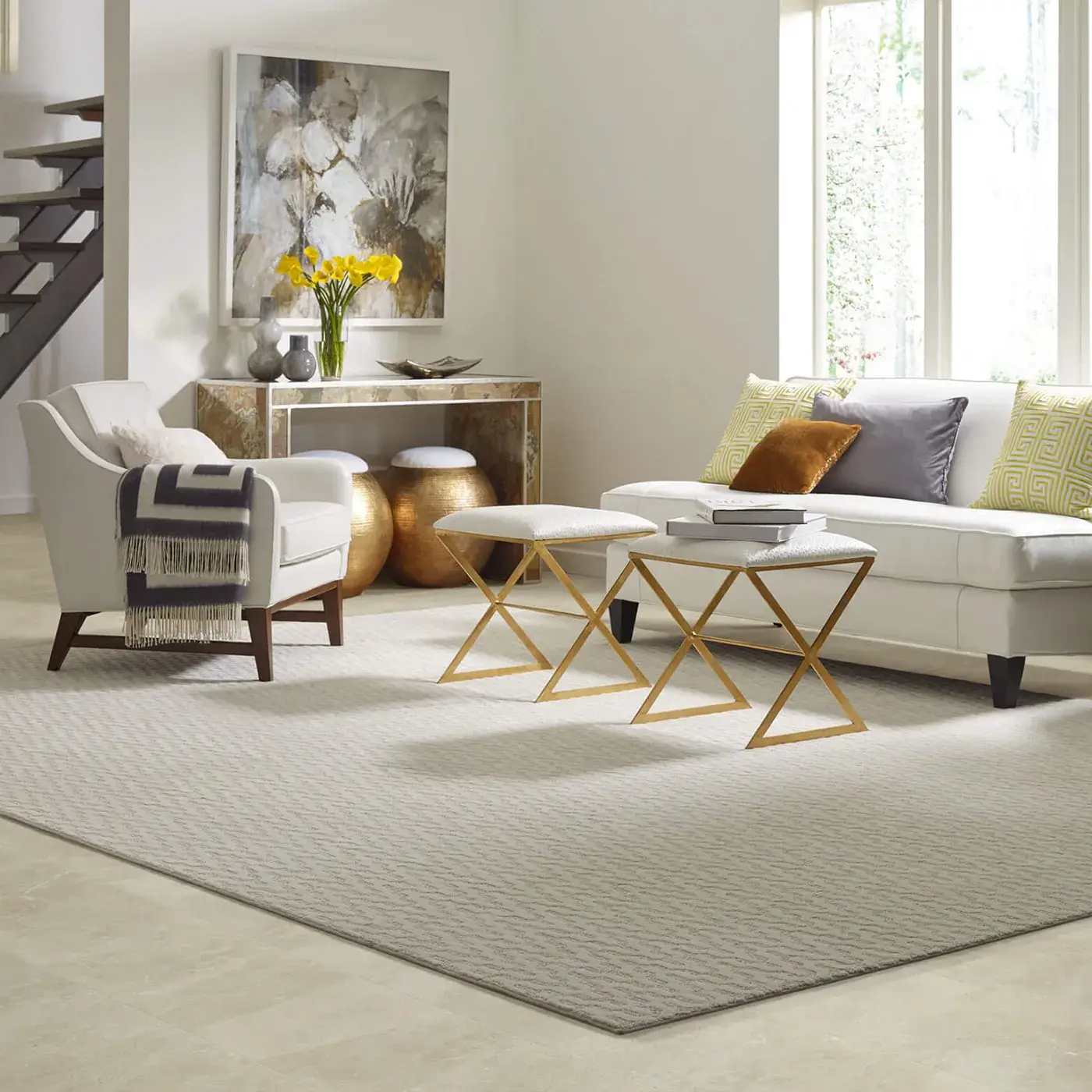 Oasis-CS72Q-00200-Beige-RUG copy A beige Shaw Floors area rug with a subtle patterned texture anchors a living room space with a white sofa, white armchairs, and gold accent tables on light-colored flooring.