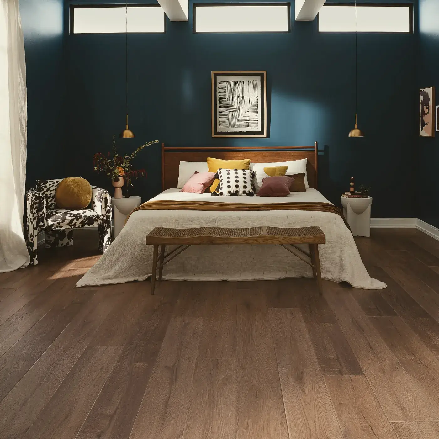 VV810_04027_ROOM COREtec Luxury Vinyl in a medium brown wood tone in a bedroom with dark blue walls and a bed with a wooden headboard.
